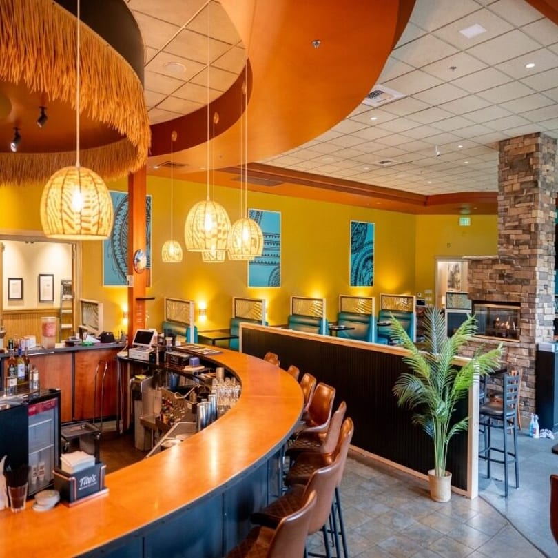 Restaurant interior with a curved bar, booths, yellow walls, and a stone fireplace.
