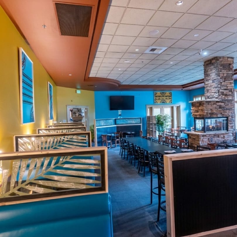 Vibrant restaurant interior with blue booths, yellow walls, a long communal table, and a stone fireplace.