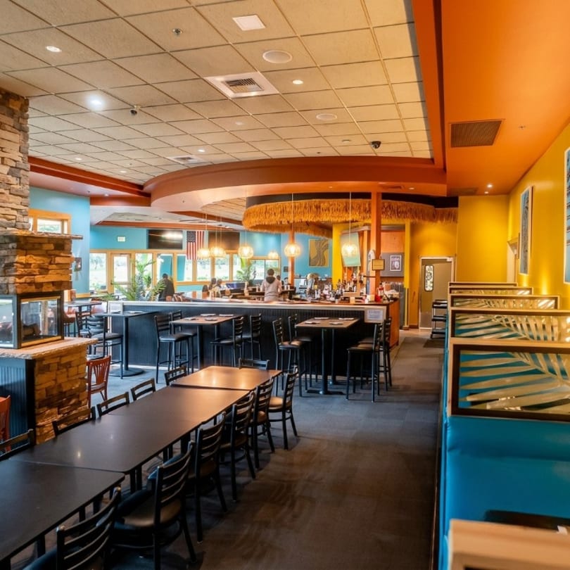 Spacious restaurant interior with a bar, dining tables, booths, and colorful tropical decor.