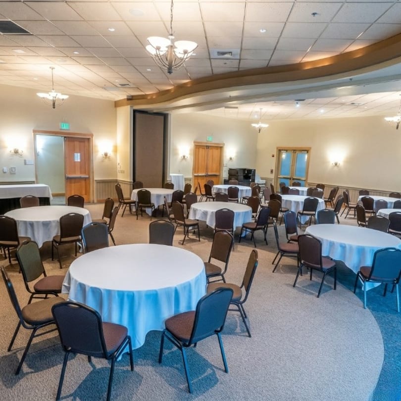 A large, empty banquet room with many round tables covered in white tablecloths and chairs.