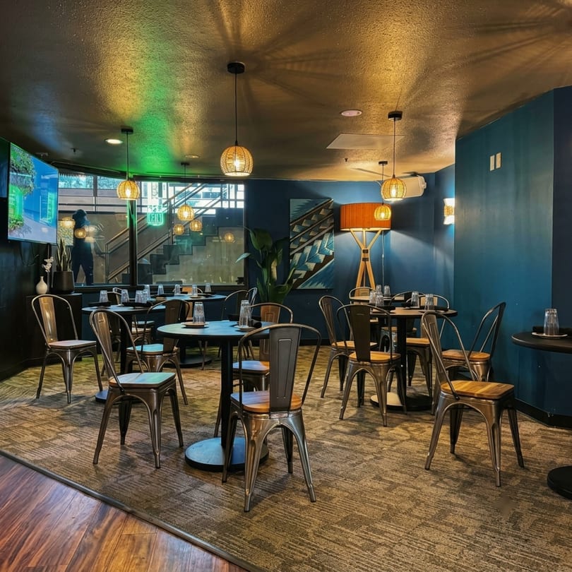 Restaurant dining room with dark blue walls, round tables, metal chairs, and woven pendant lights.
